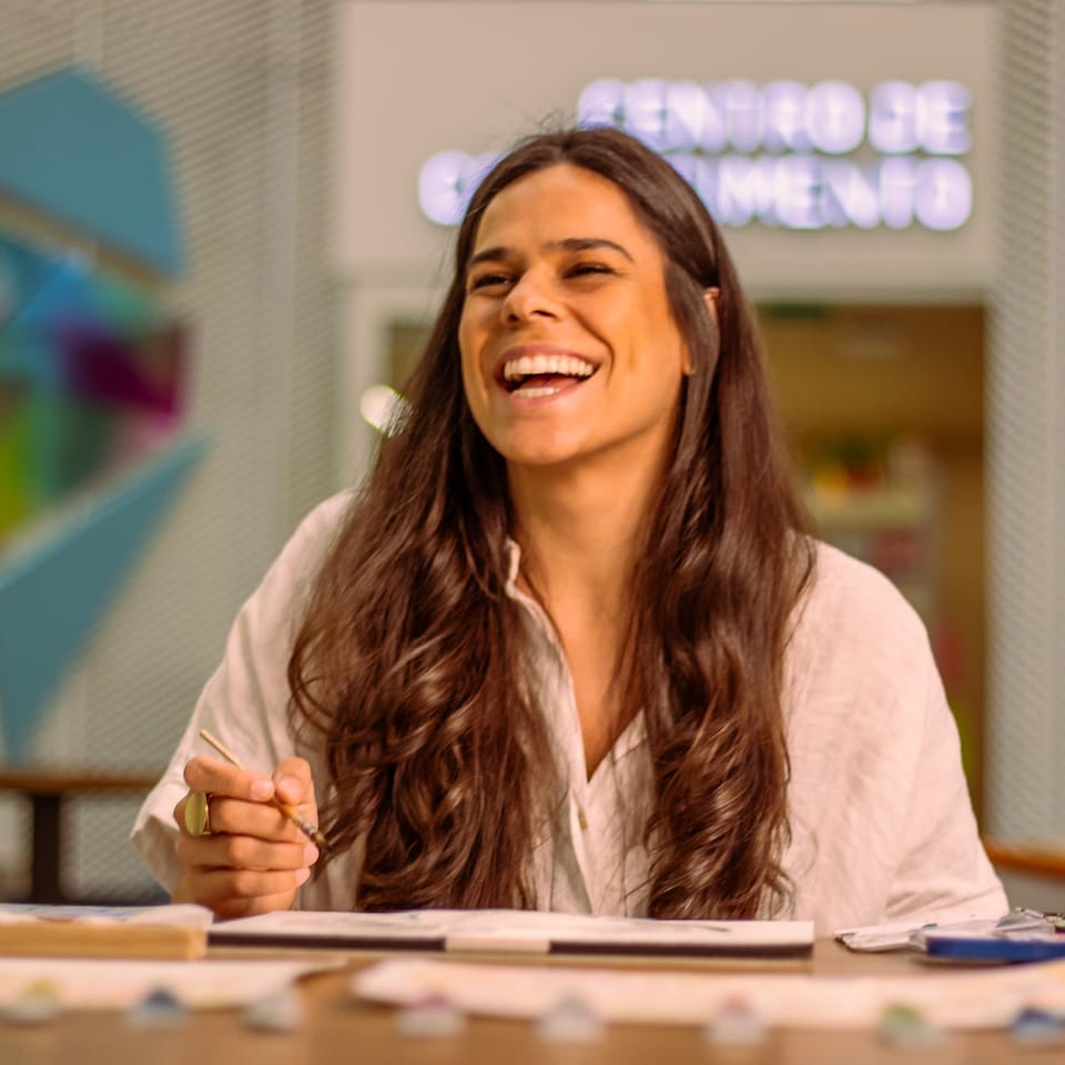 Participante sorrindo com pincel na mão durante aula de aquarela na Belas Artes