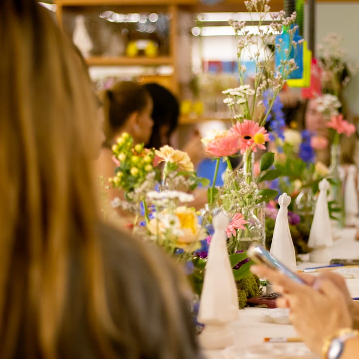 Mesa de workshop com arranjos de flores e peças para pintar