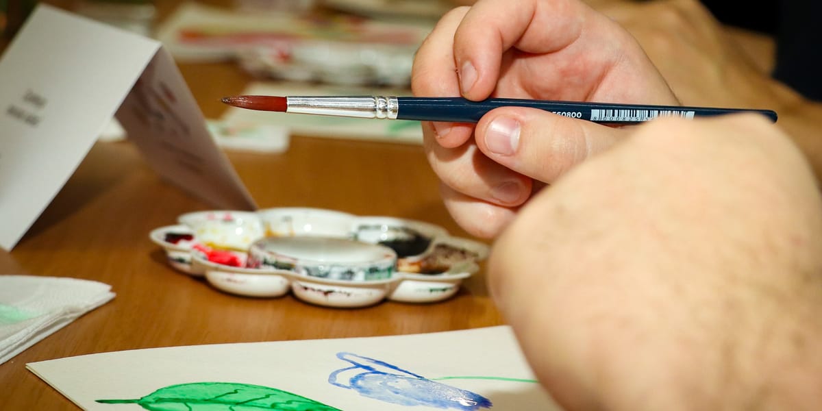 Mão segurando pincel ao lado de paleta de aquarela durante aula de pintura